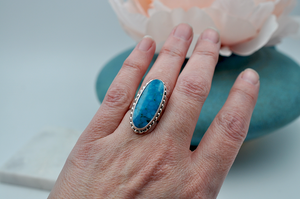 An oblong oval bright blue Kingman turquoise ring is set sterling silver is sure to stand out. US Size 7