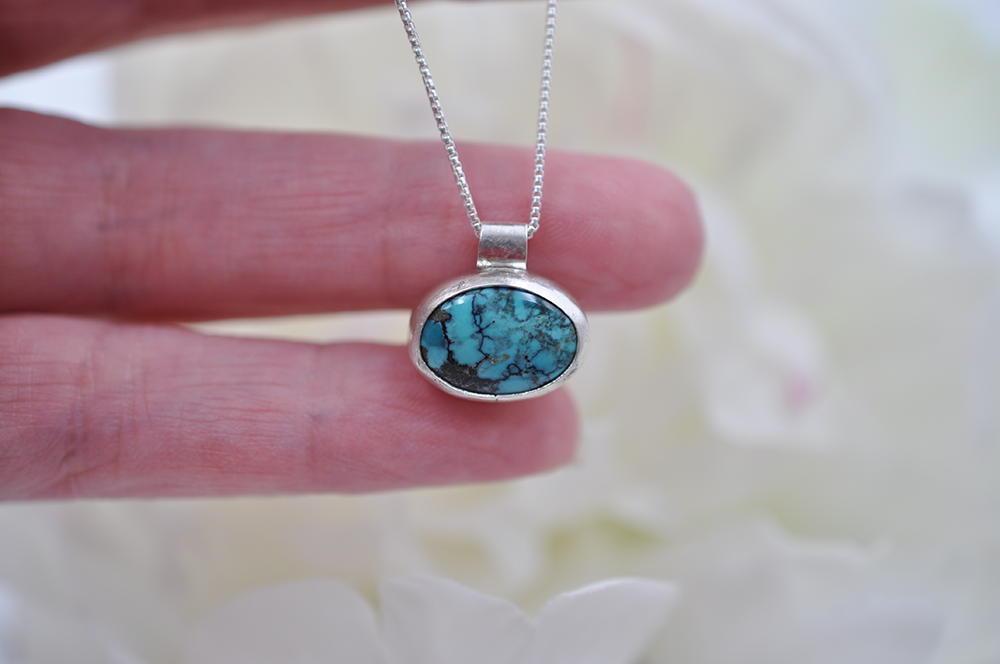 Turquoise pendant necklace held by a hand against a blurred background