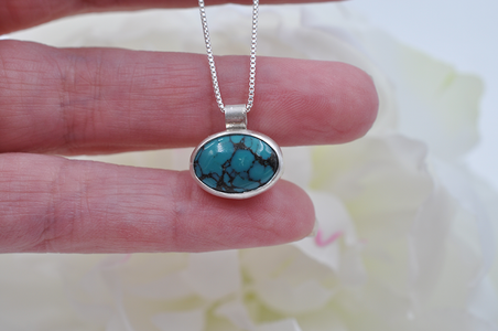 Turquoise pendant necklace held between fingers with a soft floral background