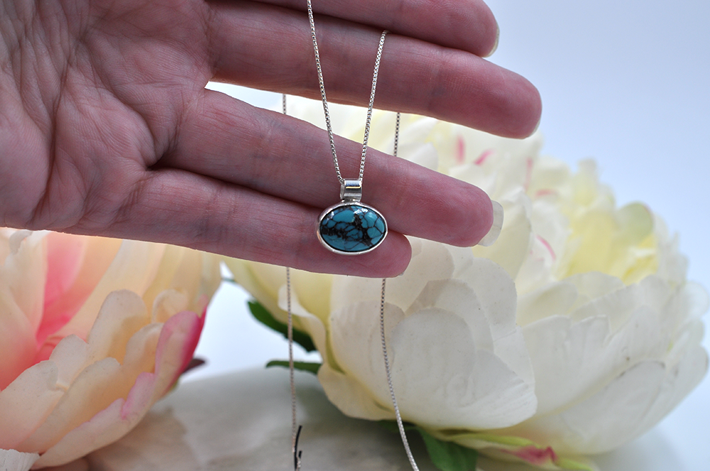 Turquoise stone pendants on silver chains held in a hand