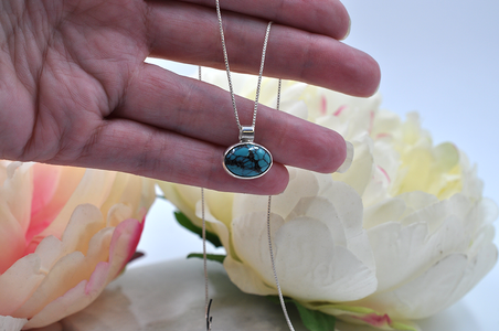Turquoise stone pendants on silver chains held in a hand