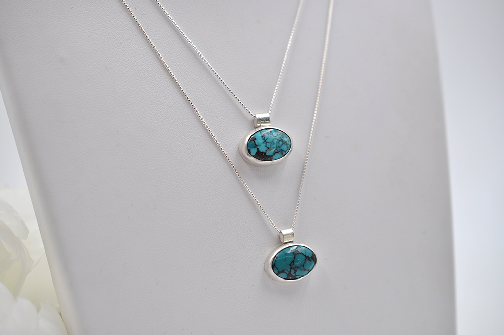 Two layered silver necklaces with turquoise horizontal oval pendants on a white background