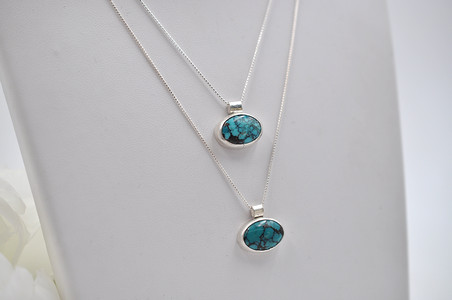 Two layered silver necklaces with turquoise horizontal oval pendants on a white background