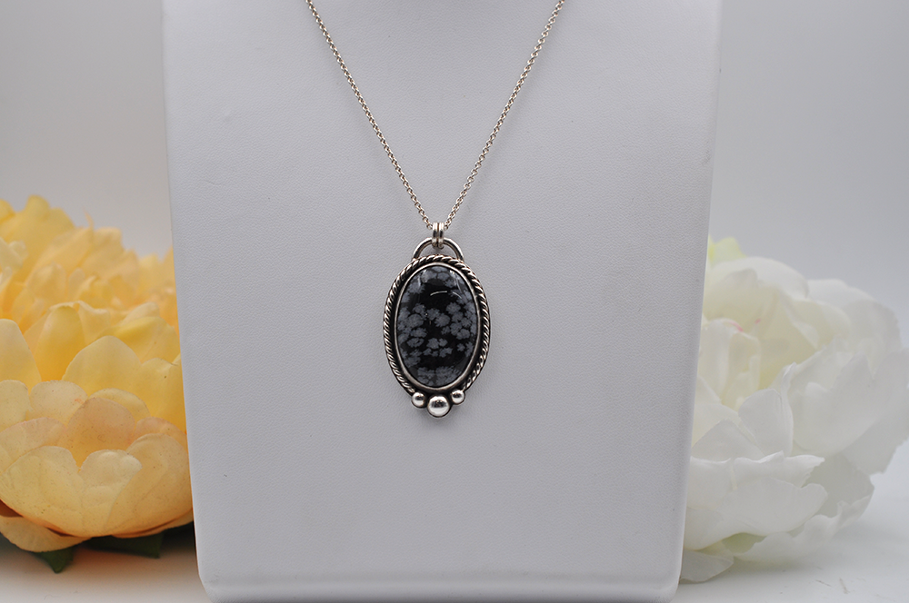 Sterling silver necklace with a black and gray pendant on a white box with flowers in the background