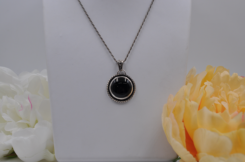 Necklace with a black onyx pendant on a white stand, surrounded by flowers