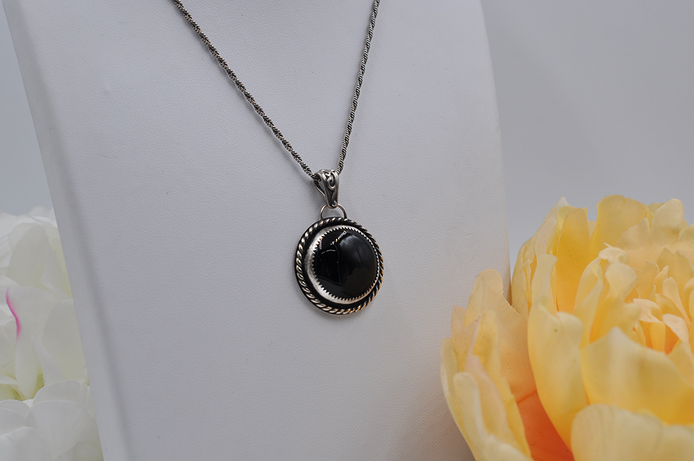 Necklace with a black onyx stone pendant on a white stand with yellow flowers.