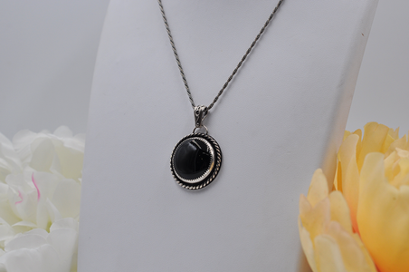 Black onyx stone pendant necklace on a white stand with flowers in the background