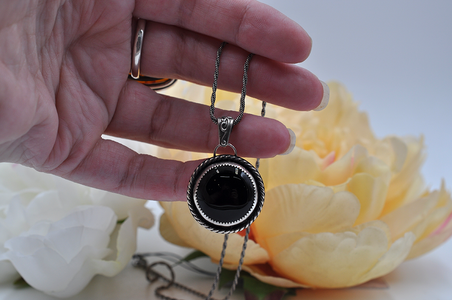 Hand holding a necklace with a black onyx pendant against a floral background
