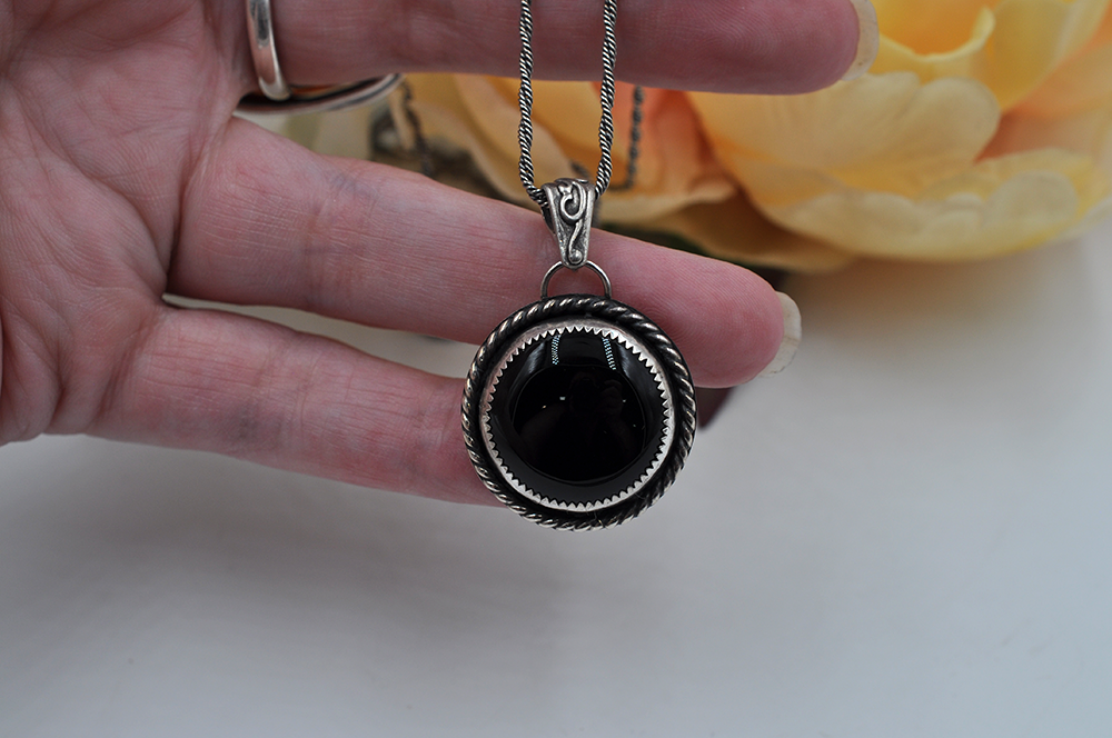 Hand holding a silver necklace with a black onyx pendant against a blurred background