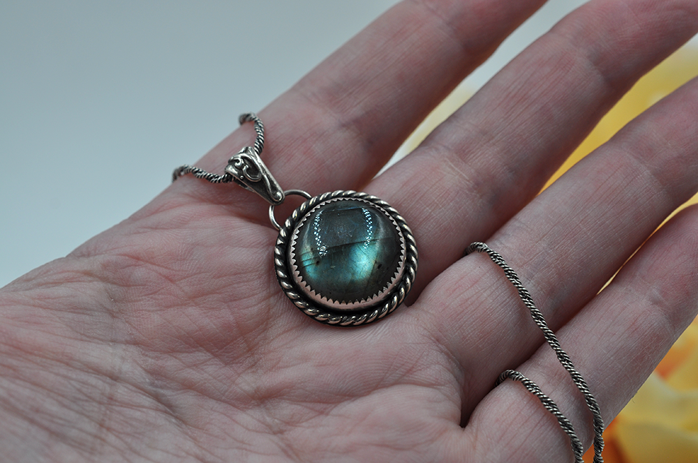 Silver pendant with a green labradorite gemstone held in a hand against a neutral background