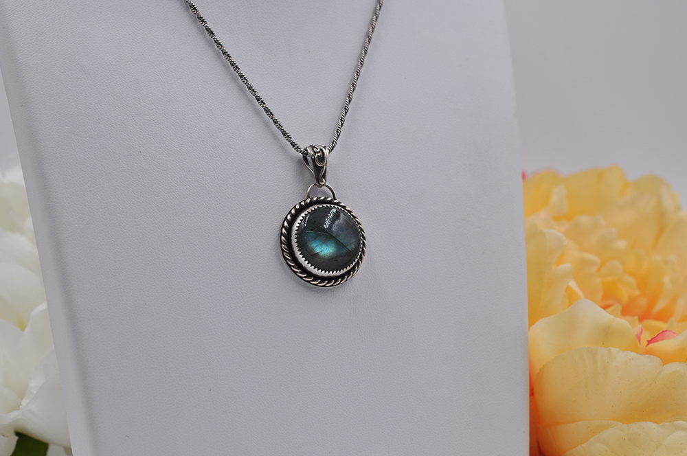 Silver necklace with a greenish-blue labradorite pendant on a white background with flowers