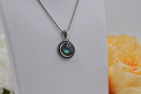 Silver necklace with a greenish-blue labradorite pendant on a white background with flowers