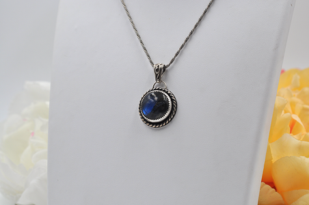 Silver necklace with a blue labradorite pendant on a white stand with floral background