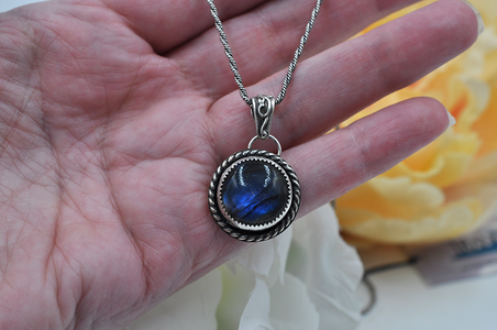 Silver pendant with blue labradorite stone held in a hand against a blurred floral background