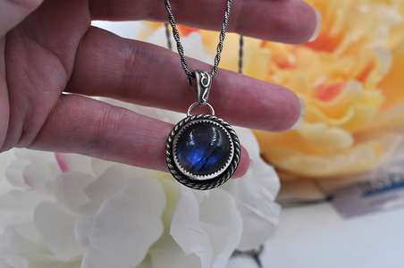 Hand holding a necklace with a blue labradorite pendant against a blurred floral background