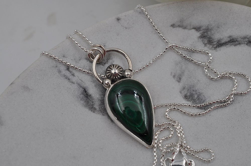 Silver necklace with a green pendant on a marble surface