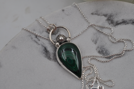 Silver necklace with a green pendant on a marble surface