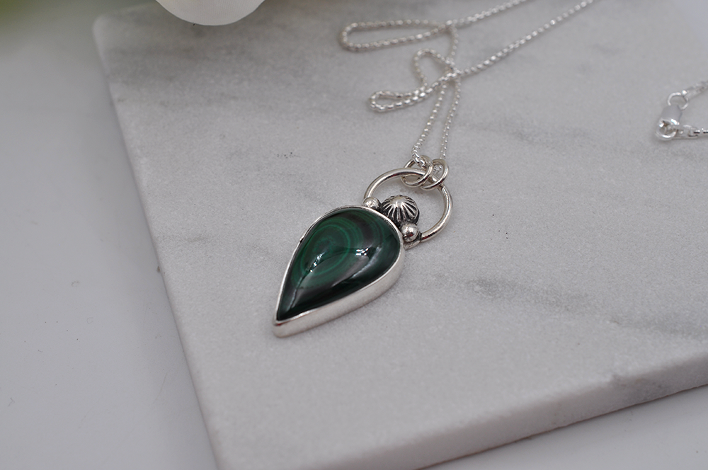 Silver necklace with a green teardrop pendant on a marble surface