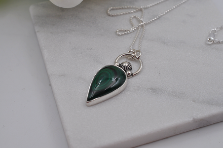 Silver necklace with a green teardrop pendant on a marble surface