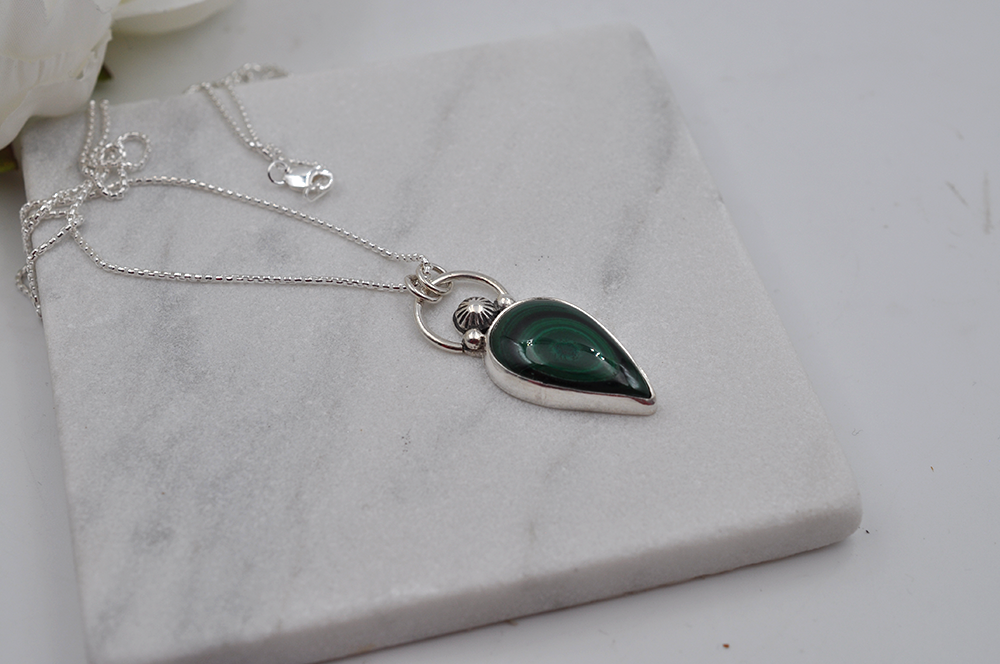 Silver necklace with a green teardrop pendant on a marble surface