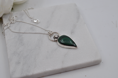 Silver necklace with a green teardrop pendant on a marble surface