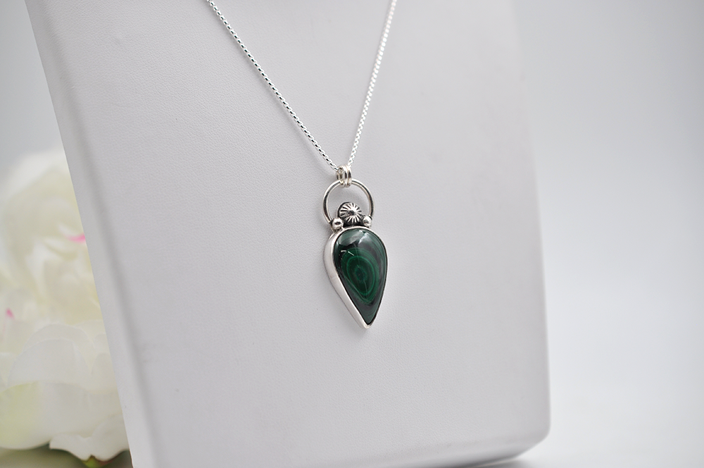 Green teardrop pendant on a silver chain against a white background