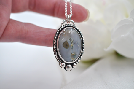 Silver necklace with a pendant held by a hand against a white background