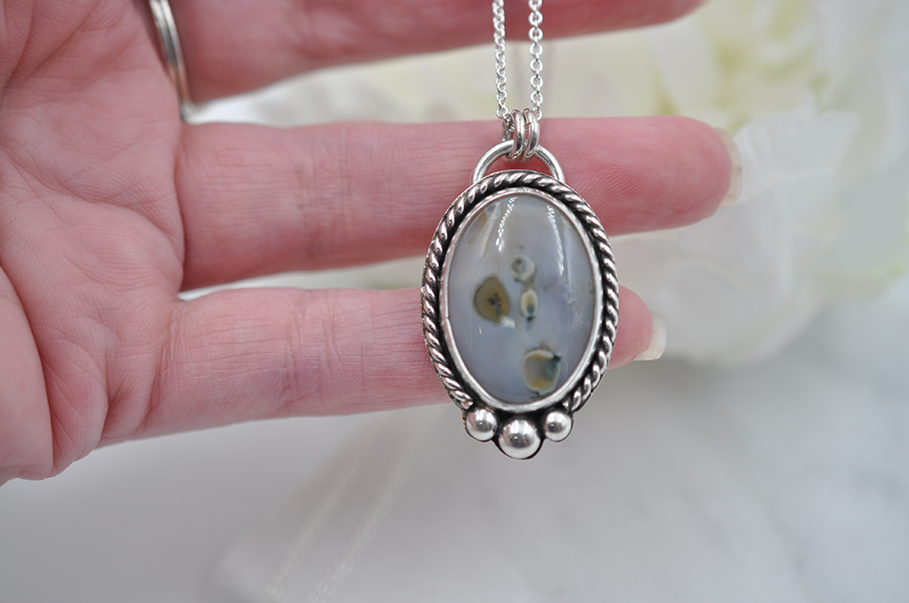 Silver pendant with a natural stone held by a hand against a blurred background