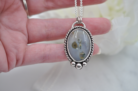 Silver pendant with a natural stone held by a hand against a blurred background