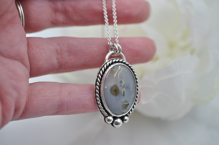 Silver necklace with an oval stone pendant held by a hand against a soft background