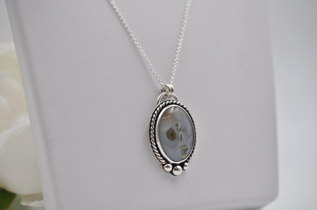 Silver necklace with an oval pendant on a white background