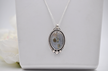 Silver necklace with an oval pendant on a white surface