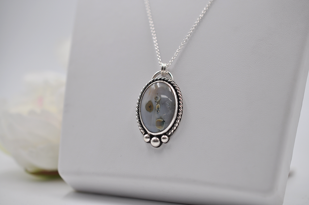Silver necklace with an oval pendant on a white surface