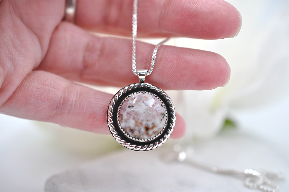 Silver necklace with a round pendant held by a hand against a blurred background