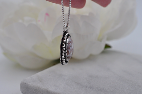 Side view of a silver necklace with a pendant held over white flowers