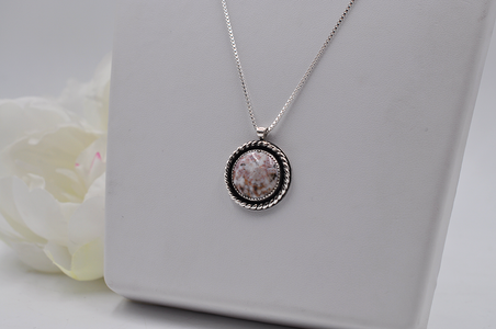 Silver necklace with a round pendant on a white surface