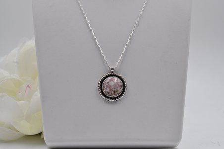 Silver necklace with a round pendant on a gray surface with a white flower.