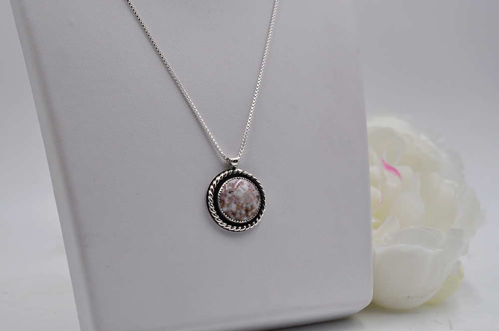 Silver necklace with a round pendant on a white surface