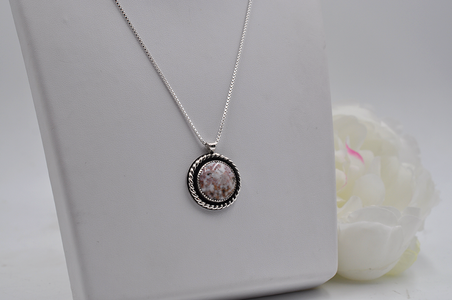 Silver necklace with a round pendant on a white surface