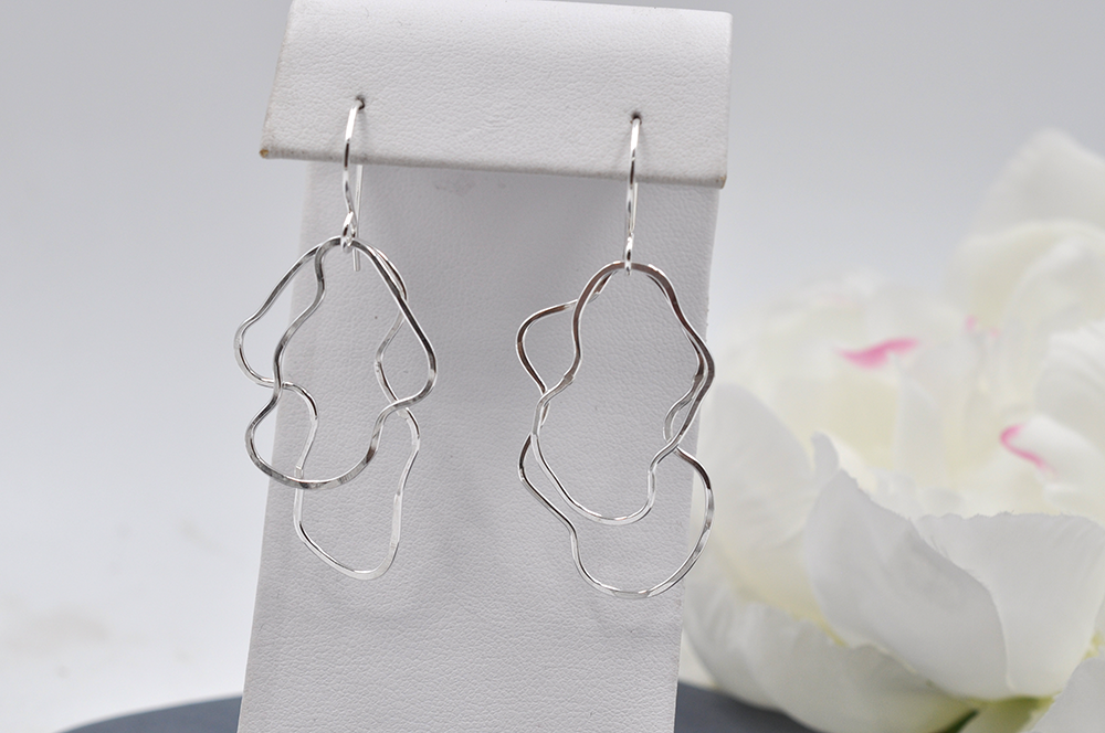 Silver abstract earrings on a white stand with a white flower in the background