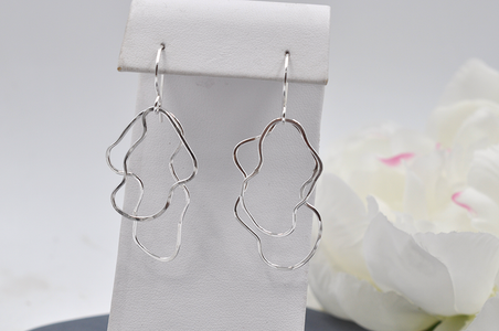 Silver abstract earrings on a white stand with a white flower in the background