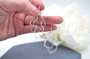 Hand holding an organic silver wire earrings with a blurred white flower in the background