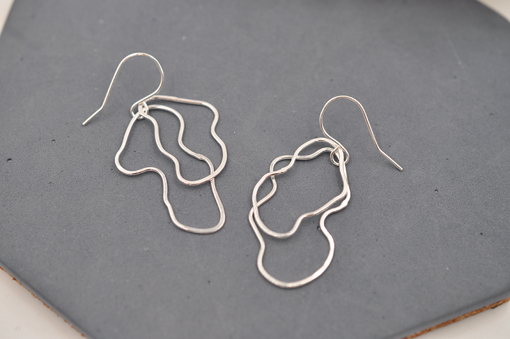 Silver abstract wire earrings on a gray surface