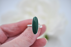 Silver ring with a green stone held in a hand against a blurred background