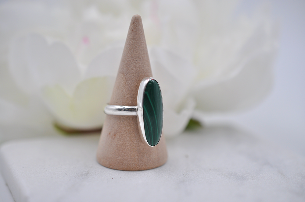 Silver ring with a green stone on a wooden cone against a blurred floral background