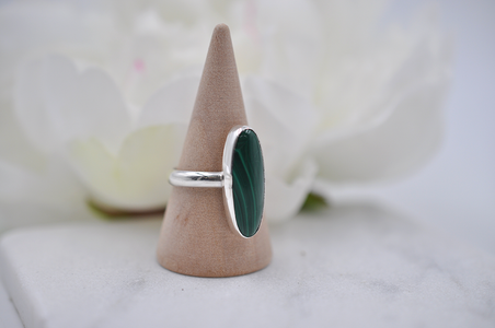 Silver ring with a green stone on a wooden cone against a blurred floral background
