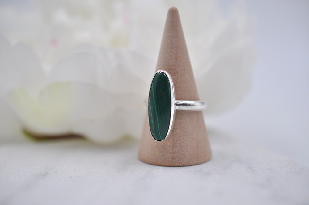 Silver ring with a green stone on a wooden cone against a white background