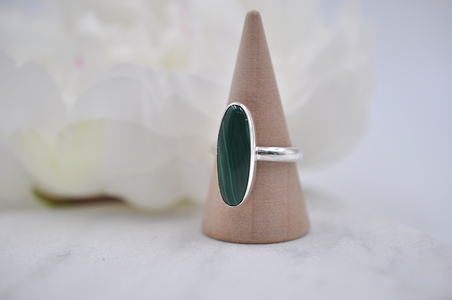 Silver ring with a green stone on a wooden cone against a white background