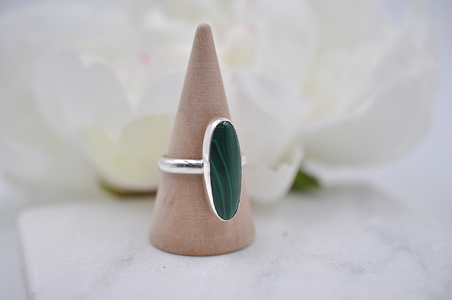 Silver ring with a green stone on a wooden cone against a soft floral background