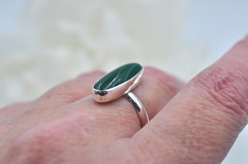 Silver ring with a green stone on a finger against a blurred background